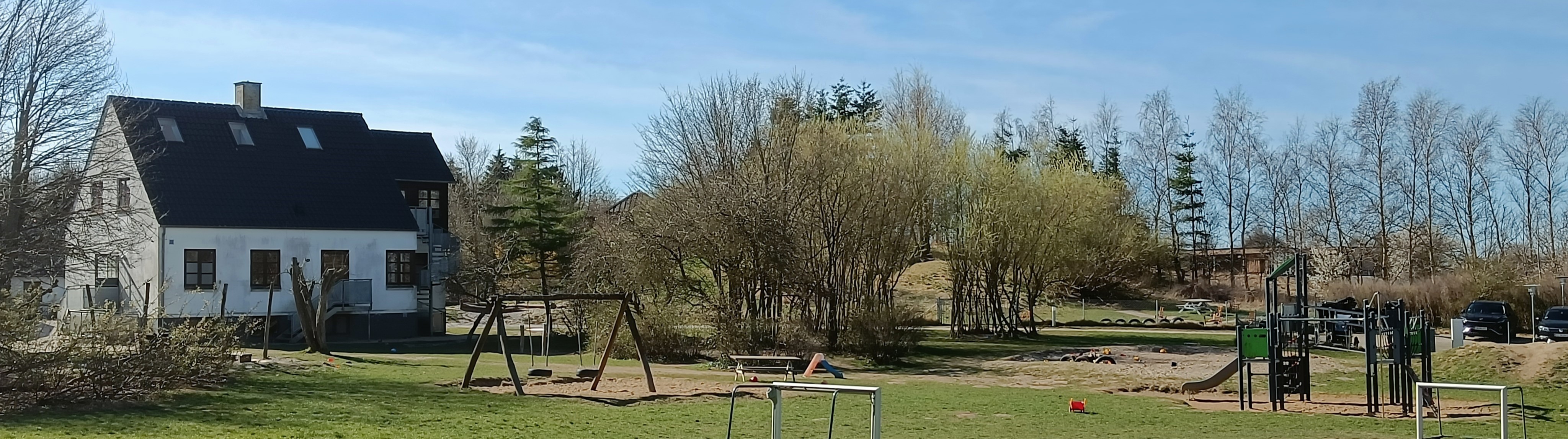 Legeplads, træer og bakker i baggrunden ved Fredensgård